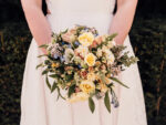 A close up of a woman in a wedding dress holds a bouquet of flowers in front of her